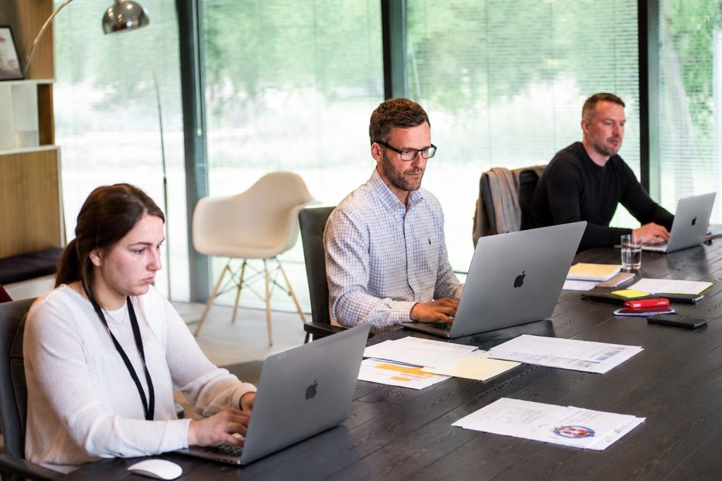 Drie collega's werken op laptops aan een vergadertafel