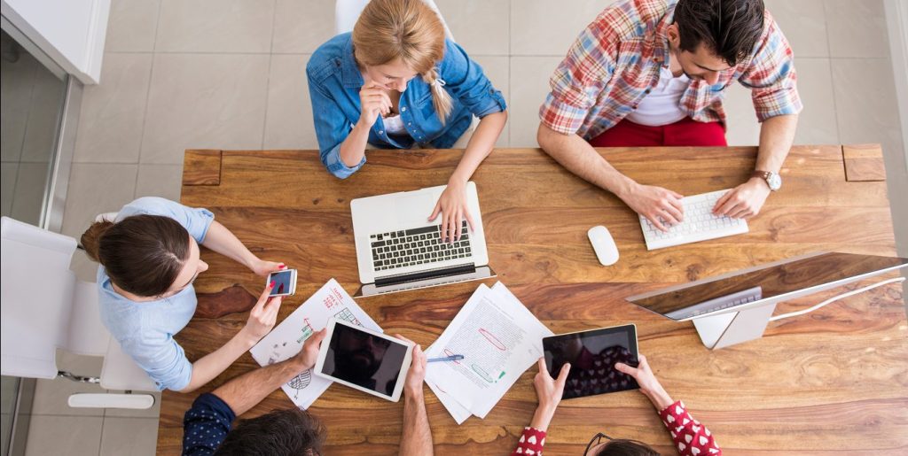 Collega's werken van bovenaf gezien aan een tafel met laptop, tablets en papieren